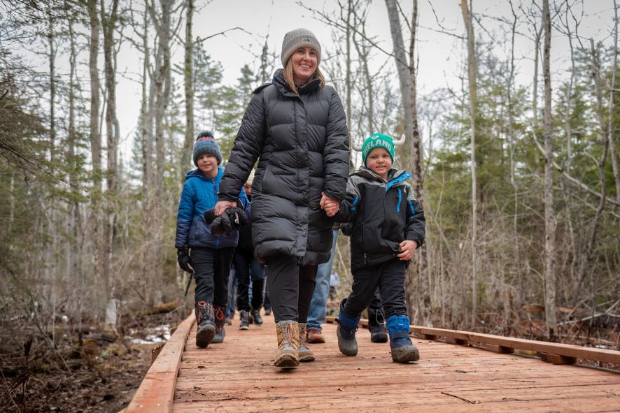 adults and children walking on boardwalk through forest