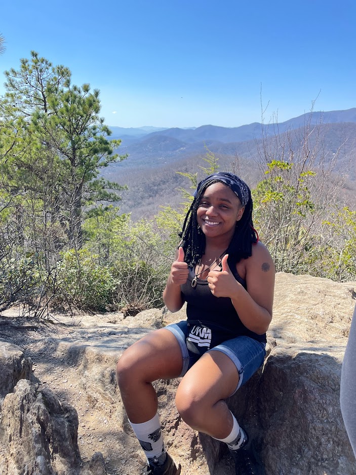 2024 Diversity in Conservation Internship cohort member holding two thumbs up while sitting on a rock during a hike