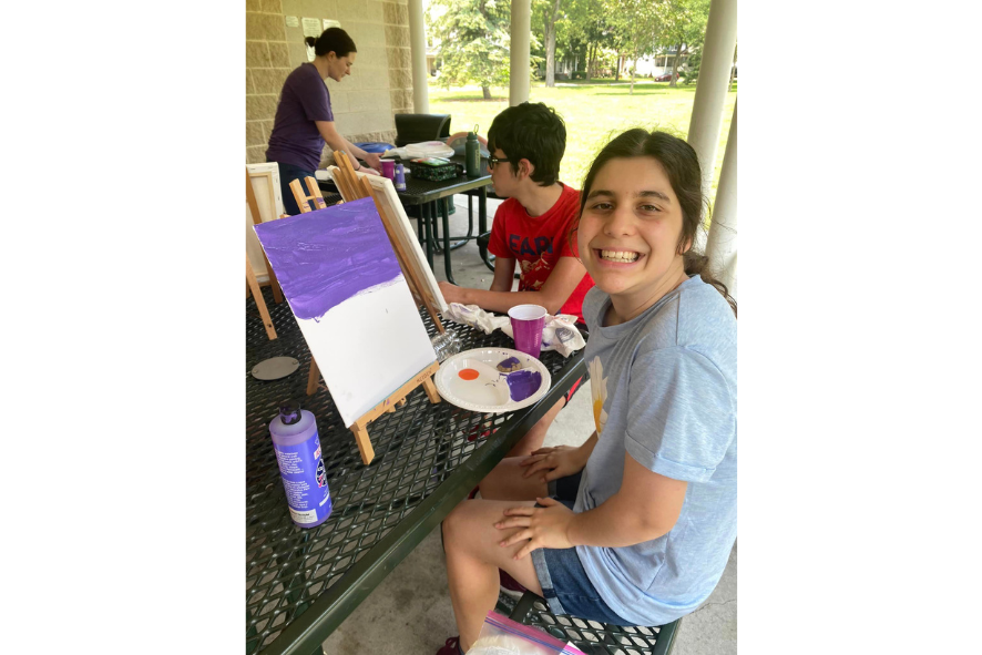 Camper smiling while painting on an easel outside