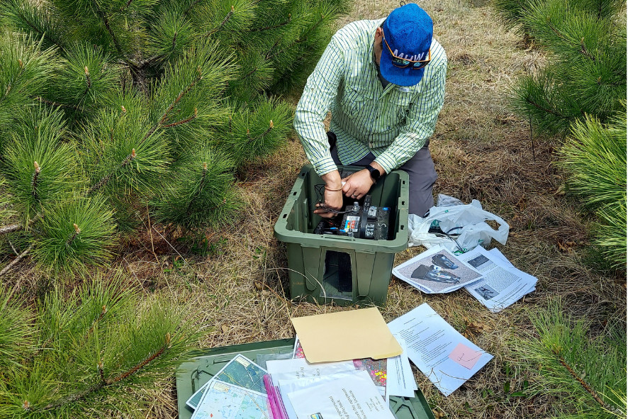 Davin kneeling on the forest floor with a bin full of field work equipment