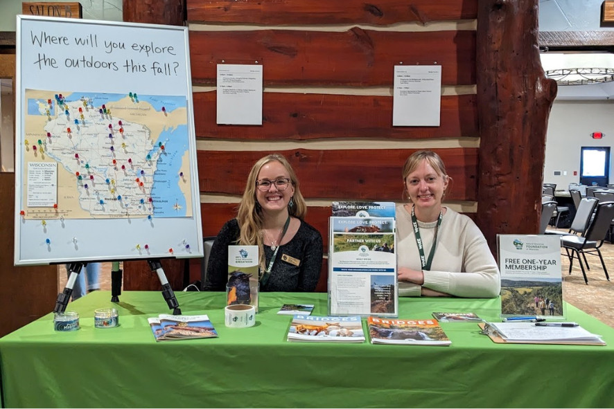 two people sitting at a table filled with promotional materials for an environmental organization, image for Cait's 10-year anniversary blog