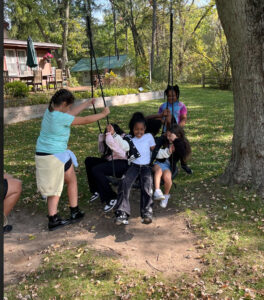 Students playing on a swing under a tree.