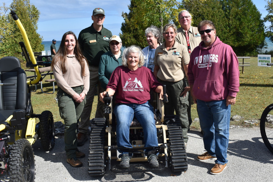 group of people standing around a person sitting in a track action wheelchair