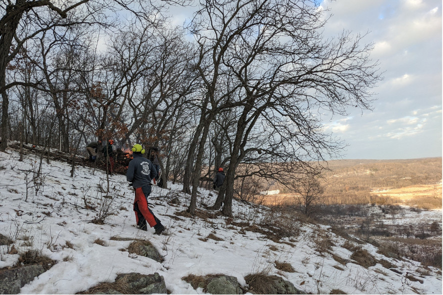 A person walking across snow-covered rocky hillside during a prescribed burn at South Bluff